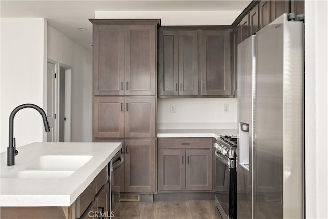 kitchen featuring dark brown cabinetry, sink, wood-type flooring, and appliances with stainless steel finishes