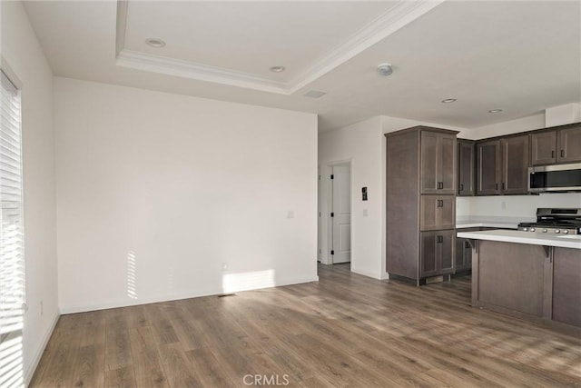 kitchen with stainless steel appliances, a raised ceiling, dark hardwood / wood-style floors, crown molding, and dark brown cabinets