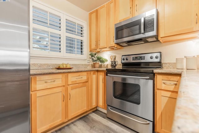 kitchen with light hardwood / wood-style floors, light stone countertops, stainless steel appliances, and light brown cabinets