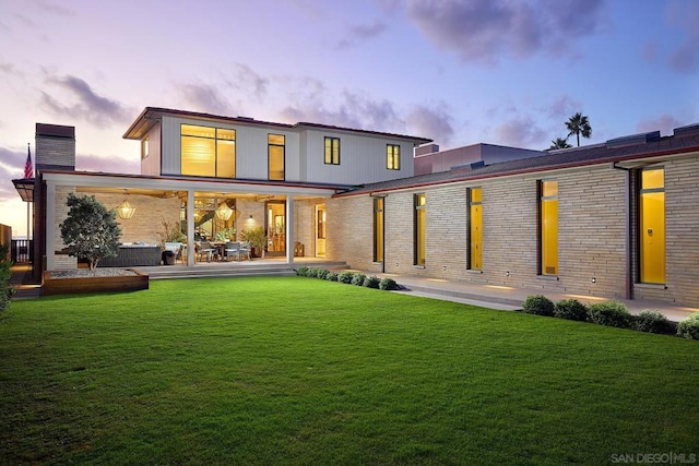 back house at dusk featuring a lawn