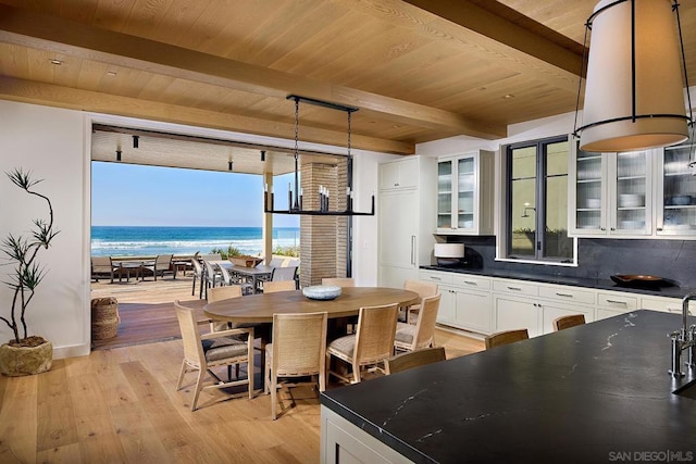 kitchen with a water view, hanging light fixtures, light hardwood / wood-style floors, beam ceiling, and white cabinetry