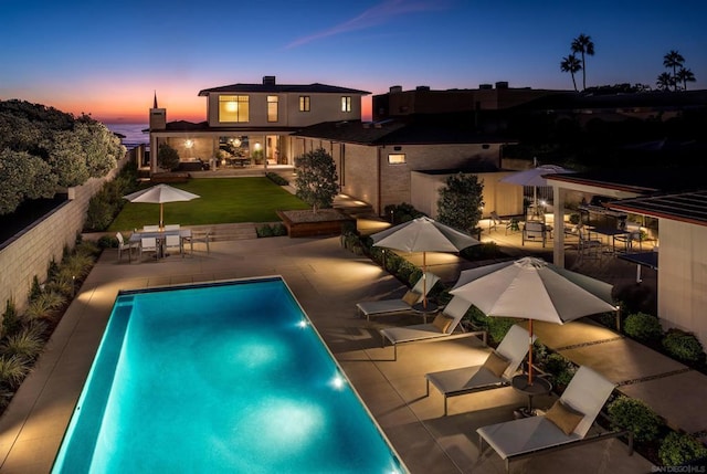 pool at dusk featuring a patio, a water view, and a lawn