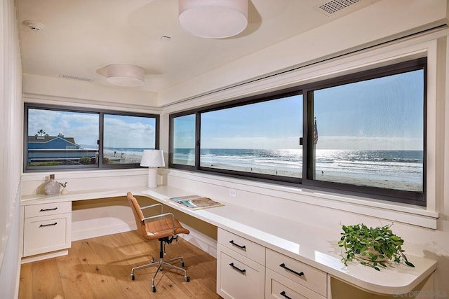 office space featuring a beach view, a water view, built in desk, and light hardwood / wood-style flooring