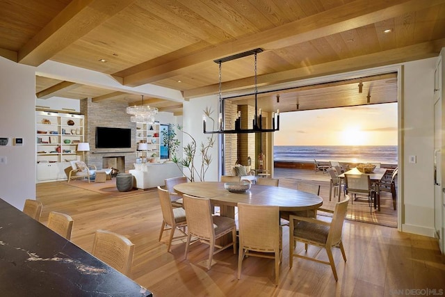 dining area featuring an inviting chandelier, a brick fireplace, light wood-type flooring, beamed ceiling, and wood ceiling