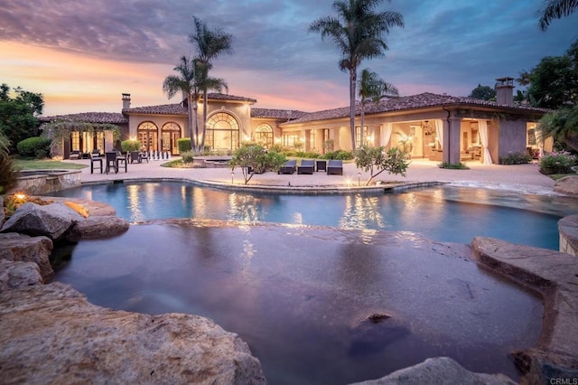 pool at dusk featuring a patio area and an in ground hot tub