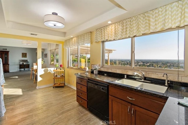 kitchen with sink, dishwasher, dark stone countertops, light hardwood / wood-style floors, and a raised ceiling