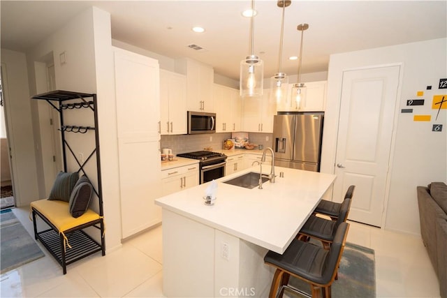 kitchen featuring appliances with stainless steel finishes, sink, decorative light fixtures, white cabinetry, and an island with sink