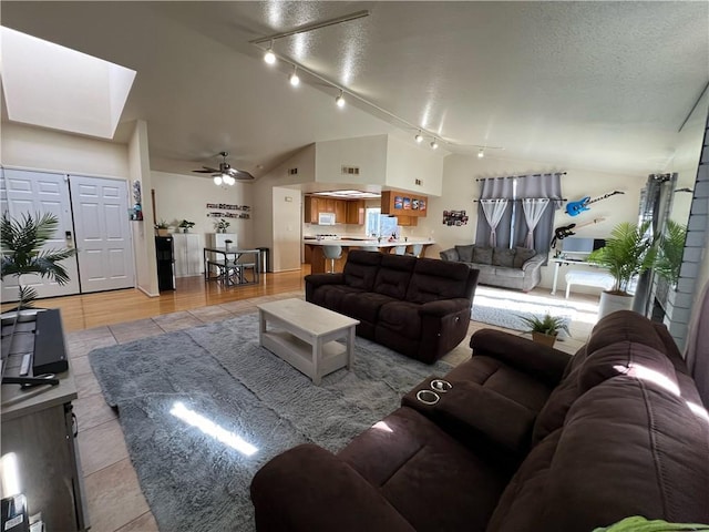 living room with ceiling fan, light hardwood / wood-style flooring, vaulted ceiling, a textured ceiling, and track lighting