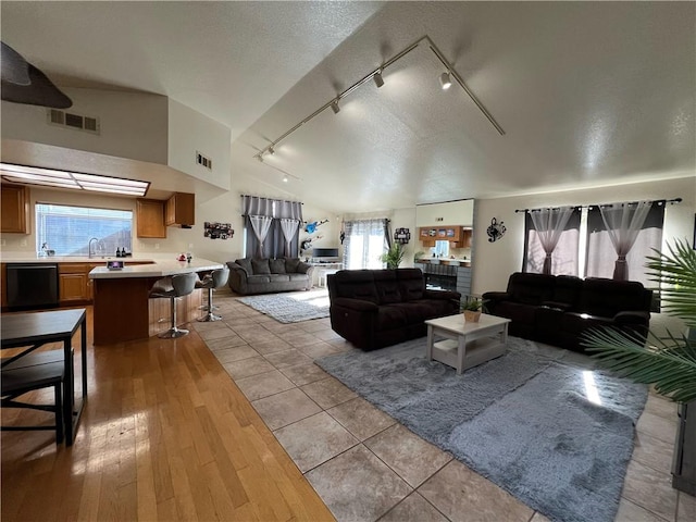 living room featuring a textured ceiling, vaulted ceiling, rail lighting, and light hardwood / wood-style flooring