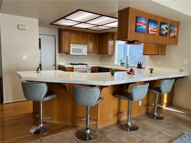 kitchen with a breakfast bar area, kitchen peninsula, white appliances, and light wood-type flooring