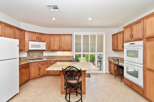 kitchen featuring a breakfast bar, white appliances, light tile patterned floors, a kitchen island, and light stone counters