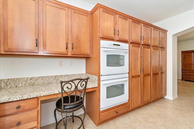 kitchen featuring white double oven, built in desk, light stone counters, and light tile patterned floors