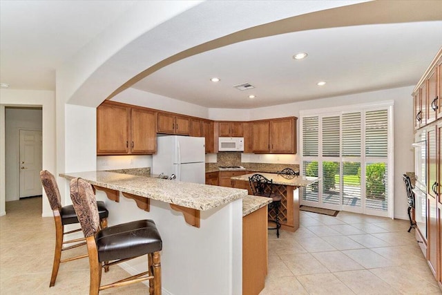 kitchen featuring a breakfast bar area, kitchen peninsula, light tile patterned floors, and white appliances