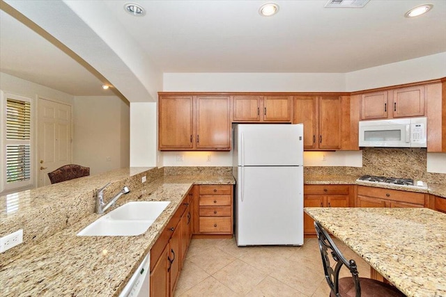 kitchen featuring kitchen peninsula, light stone countertops, sink, and white appliances