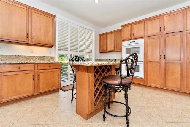 kitchen with a breakfast bar, light tile patterned floors, light stone counters, and double oven