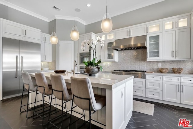 kitchen featuring decorative light fixtures, stainless steel appliances, tasteful backsplash, and a center island with sink