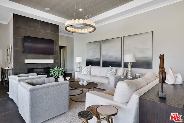 tiled living room featuring a tiled fireplace, crown molding, and a chandelier