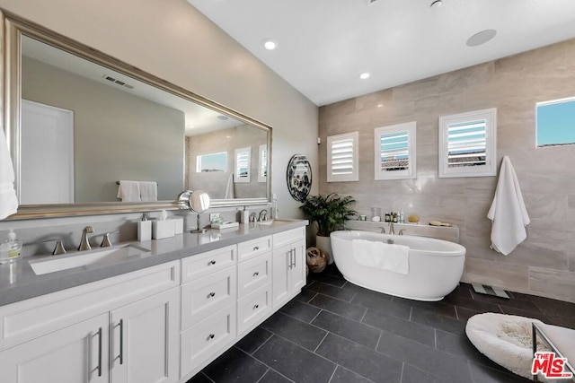 bathroom featuring tile patterned flooring, vanity, tile walls, and a bathing tub