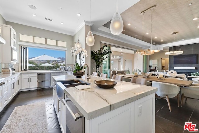 kitchen featuring a kitchen island with sink, tasteful backsplash, decorative light fixtures, light stone counters, and white cabinetry