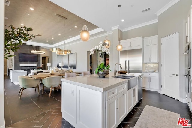 kitchen featuring a center island with sink, a raised ceiling, hanging light fixtures, light stone counters, and white cabinetry