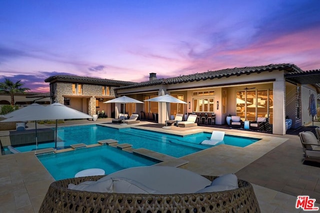 pool at dusk featuring an in ground hot tub, an outdoor living space, and a patio