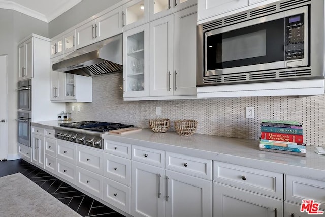 kitchen featuring decorative backsplash, appliances with stainless steel finishes, light stone counters, ornamental molding, and white cabinetry