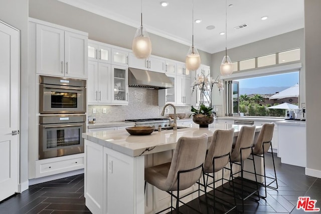 kitchen featuring white cabinets, decorative backsplash, stainless steel double oven, and a kitchen island with sink