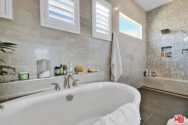 bathroom with a tub to relax in, tile patterned flooring, and tile walls