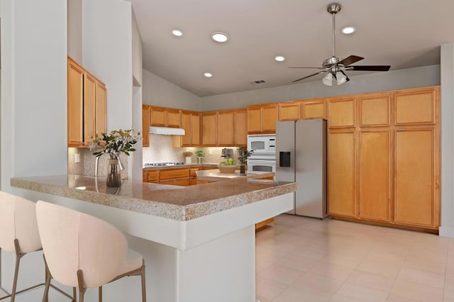 kitchen with white appliances, a kitchen breakfast bar, vaulted ceiling, ceiling fan, and kitchen peninsula