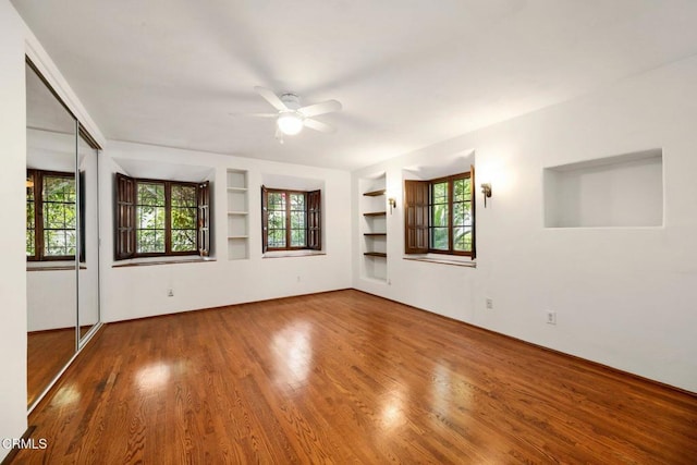 unfurnished room featuring hardwood / wood-style flooring, ceiling fan, and built in shelves