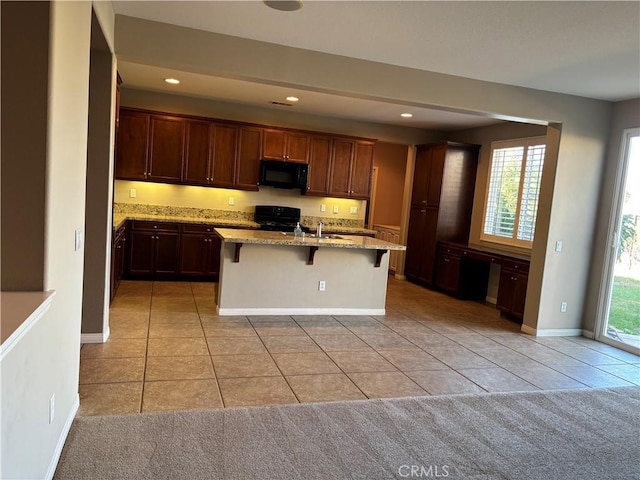 kitchen featuring black appliances, a kitchen bar, a center island with sink, and a wealth of natural light