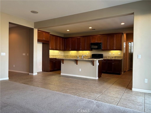 kitchen featuring light carpet, light stone counters, a breakfast bar, black appliances, and a center island with sink