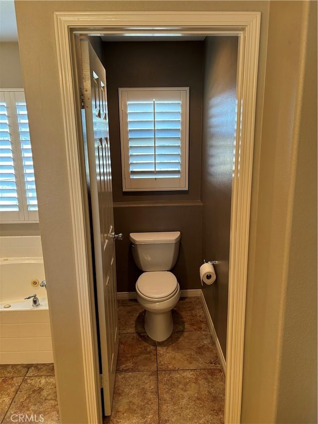 bathroom featuring tile patterned flooring, toilet, plenty of natural light, and tiled tub