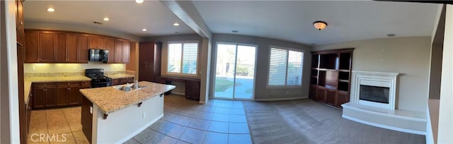 kitchen featuring a kitchen bar, light stone counters, beamed ceiling, black gas stove, and an island with sink