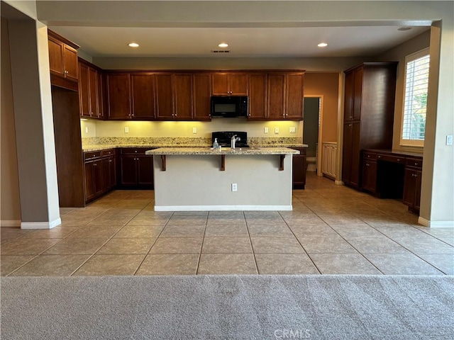 kitchen with light stone countertops, sink, a kitchen breakfast bar, a center island with sink, and light tile patterned flooring