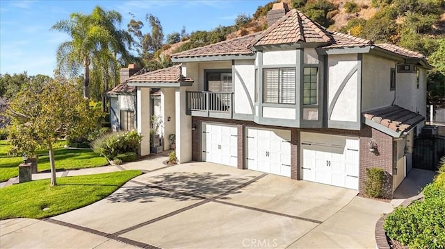 view of front of house with an attached garage, a balcony, driveway, stucco siding, and a chimney