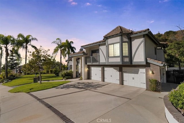 english style home with brick siding, stucco siding, a balcony, a garage, and driveway