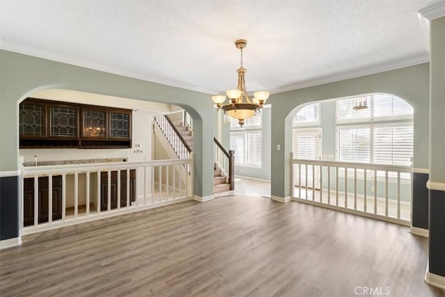 empty room featuring wood finished floors, baseboards, stairs, ornamental molding, and an inviting chandelier