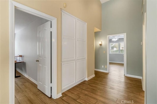 hall with light wood-type flooring, a towering ceiling, and baseboards