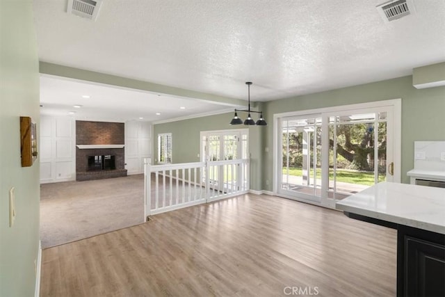 unfurnished dining area with a textured ceiling, light wood finished floors, a fireplace, and visible vents