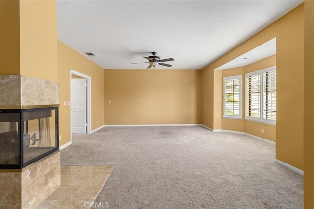 unfurnished living room with ceiling fan, light colored carpet, visible vents, baseboards, and a tiled fireplace