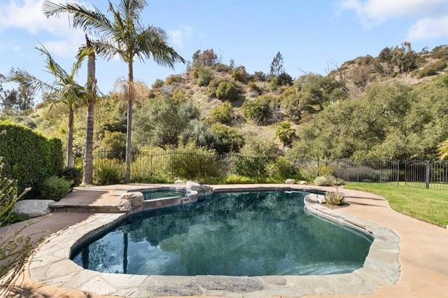 view of swimming pool featuring fence and a pool with connected hot tub