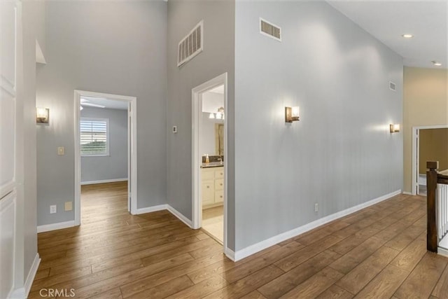 hallway with a towering ceiling, baseboards, visible vents, and wood finished floors