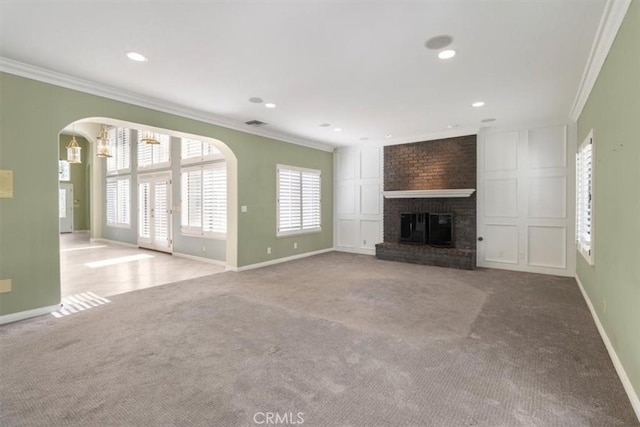 unfurnished living room featuring arched walkways, ornamental molding, a brick fireplace, light carpet, and baseboards