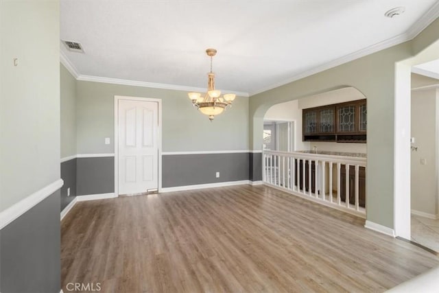 empty room featuring a chandelier, wood finished floors, visible vents, baseboards, and crown molding