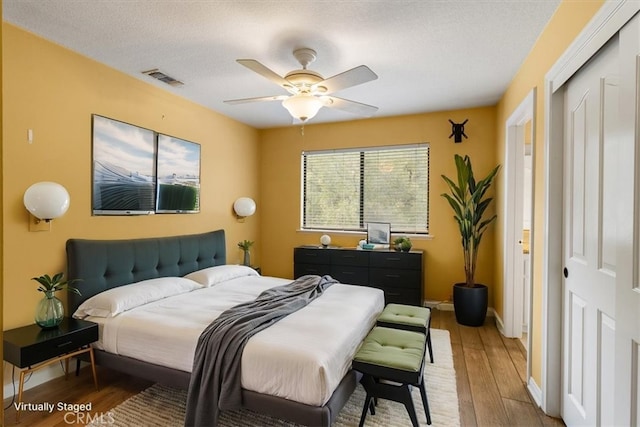 bedroom with baseboards, visible vents, ceiling fan, wood finished floors, and a textured ceiling