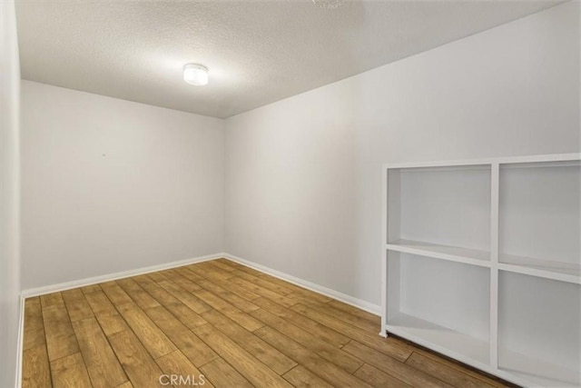 unfurnished room with a textured ceiling, wood finished floors, and baseboards