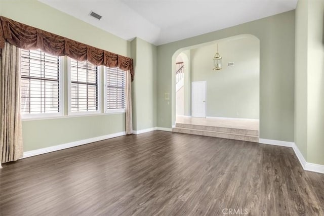 unfurnished room featuring arched walkways, visible vents, dark wood finished floors, and baseboards