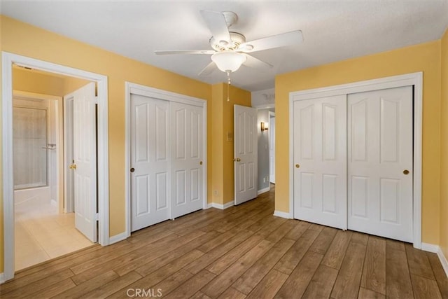 unfurnished bedroom with baseboards, light wood-style flooring, and multiple closets