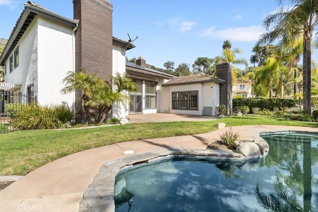 back of property featuring a lawn, a patio, a chimney, and stucco siding